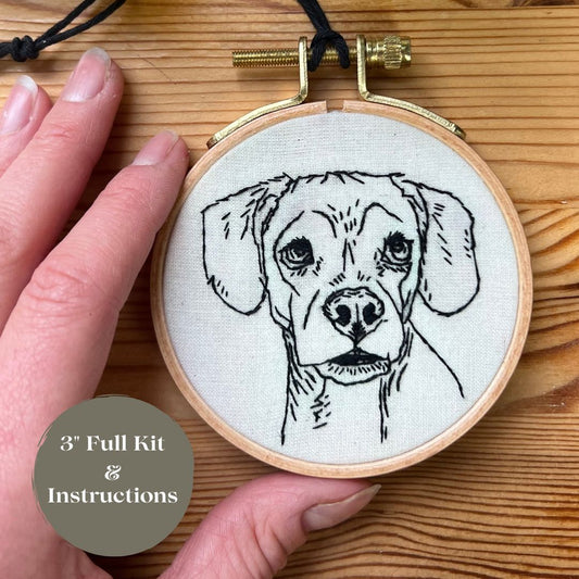 A 3" embroidery of a beagle mix dog in black thread on off-white fabric