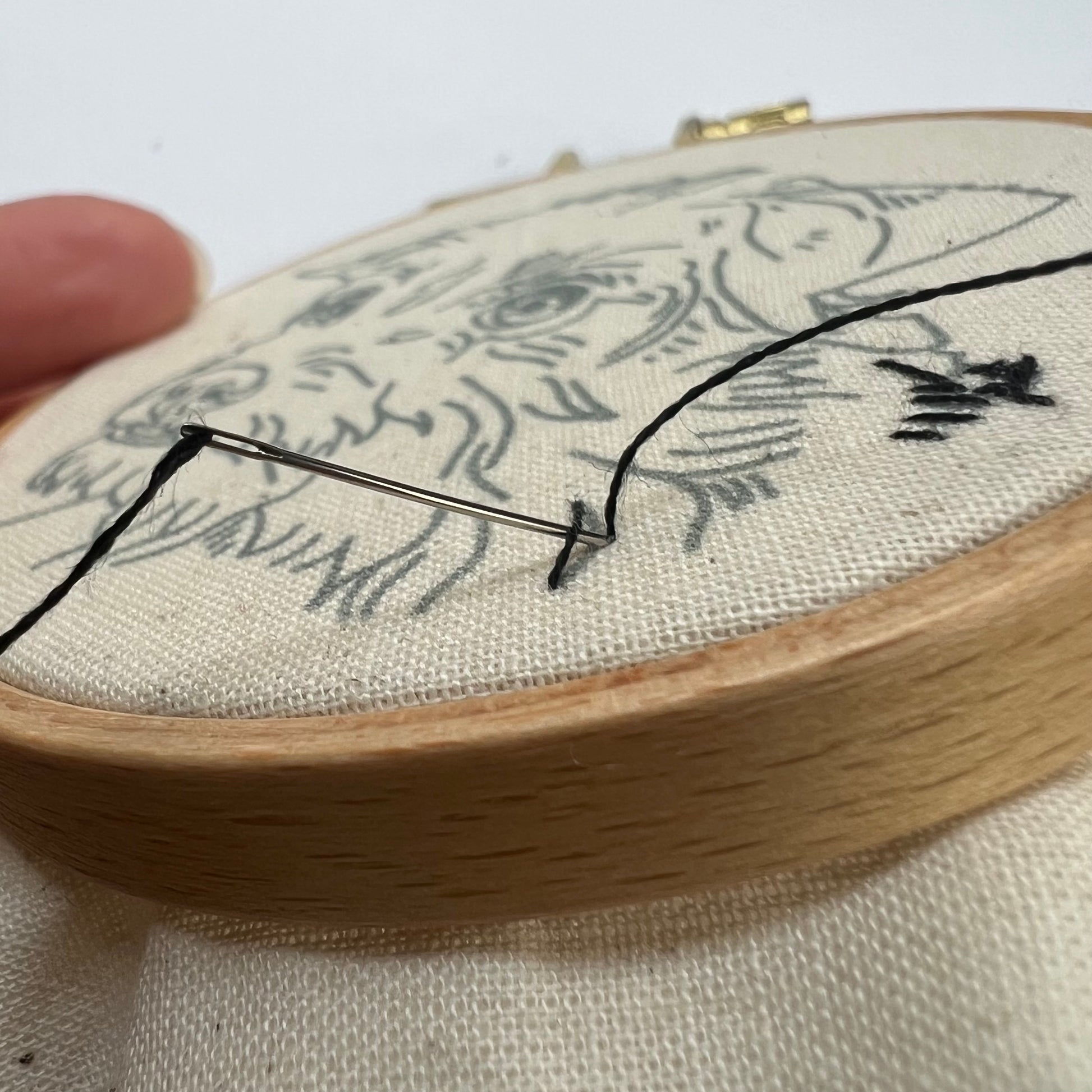 An up close image of an embroidered pet portrait work in progress with a needle and black thread going through off white fabric